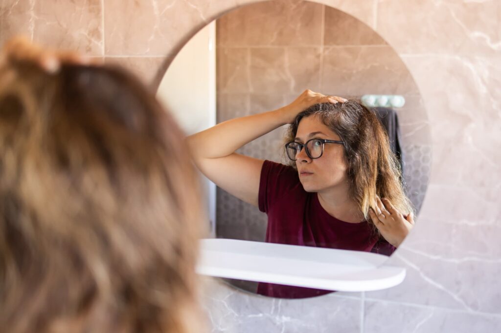 A woman examines her hair loss in the mirror