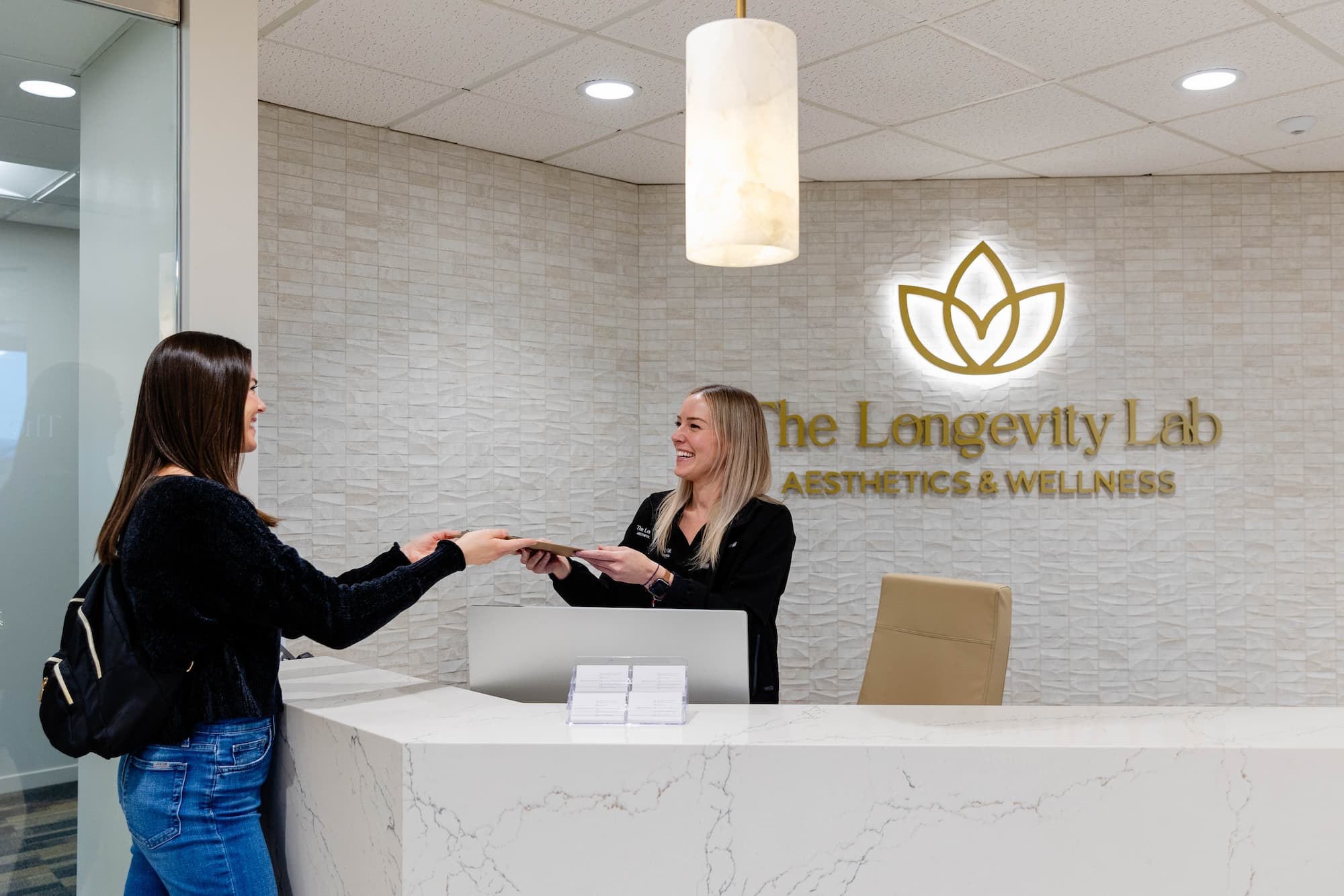 The front desk worker at The Longevity Lab handing a clipboard to a client to begin evaluating her Health and Wellness in Denver