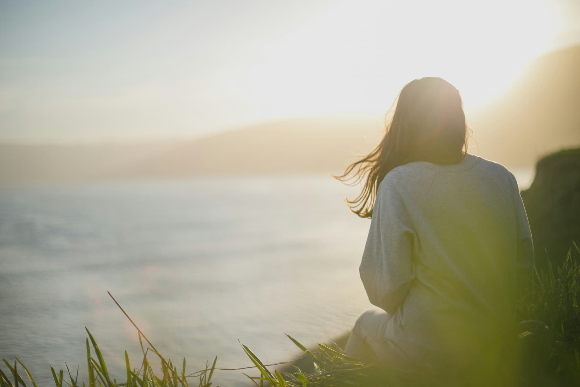 A girl sitting on a ledge watching the ocean