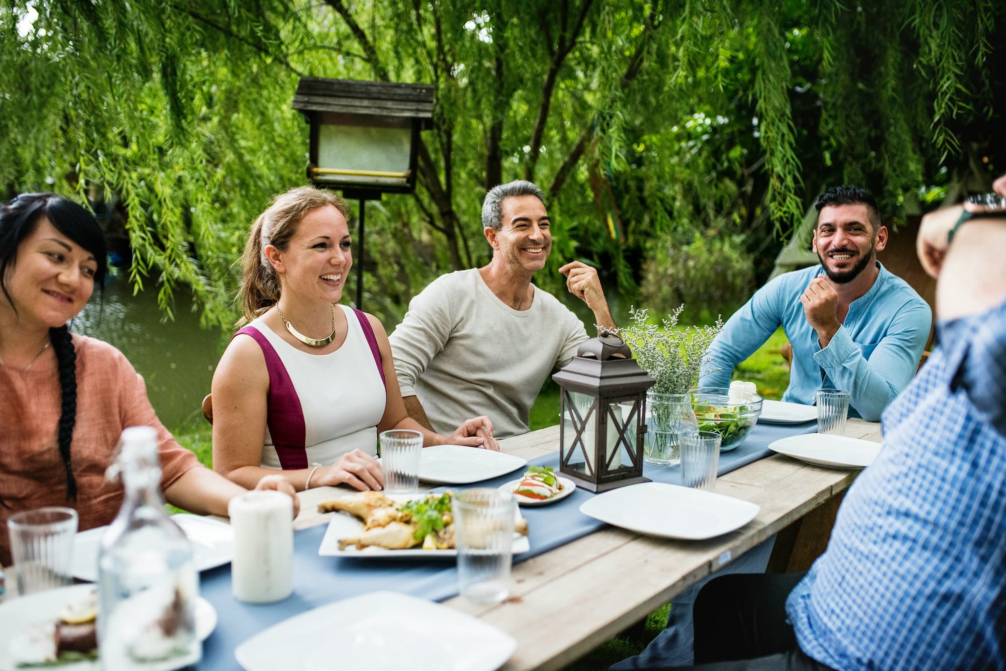 A group of adult friends enjoying one anothers company at a dining table outdoors